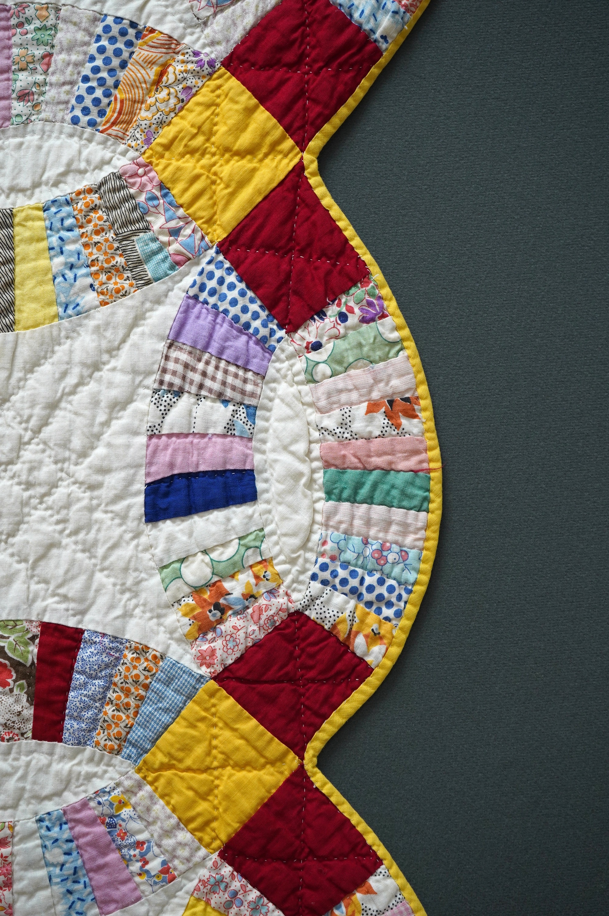 A 1940’s hand made ‘Double Wedding Ring’ patchwork quilt, made from bright multi-coloured floral and plain cotton dress fabrics into a patchwork design of large all over interlocking rings with a scalloped bright yellow